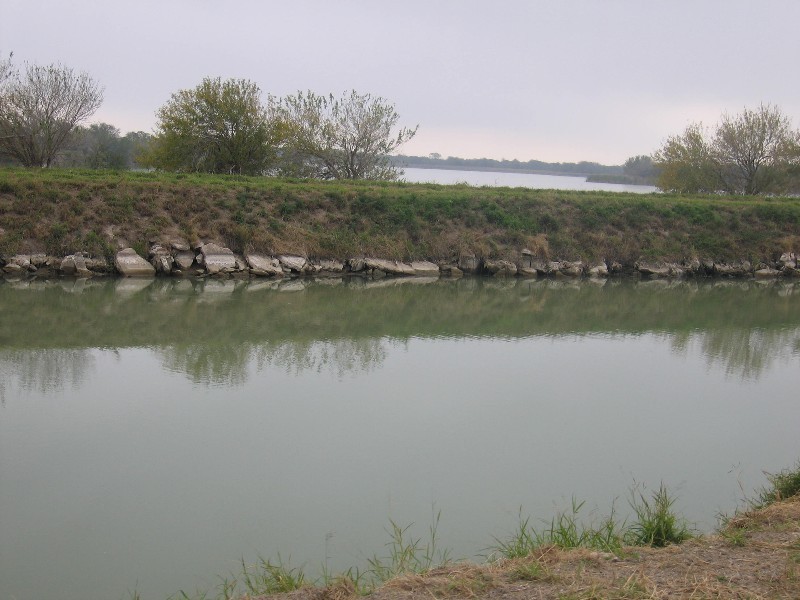 The current electric pump station raises water 42 feet from the Rio Grande River to this canal.  The water flows into the holding lake behind the canal wall in the photo.  From there the water flows in an underground canal, 15 miles to Edinburg , Texas. Once the water has been pumped out of the river, gravity moves it inland. 